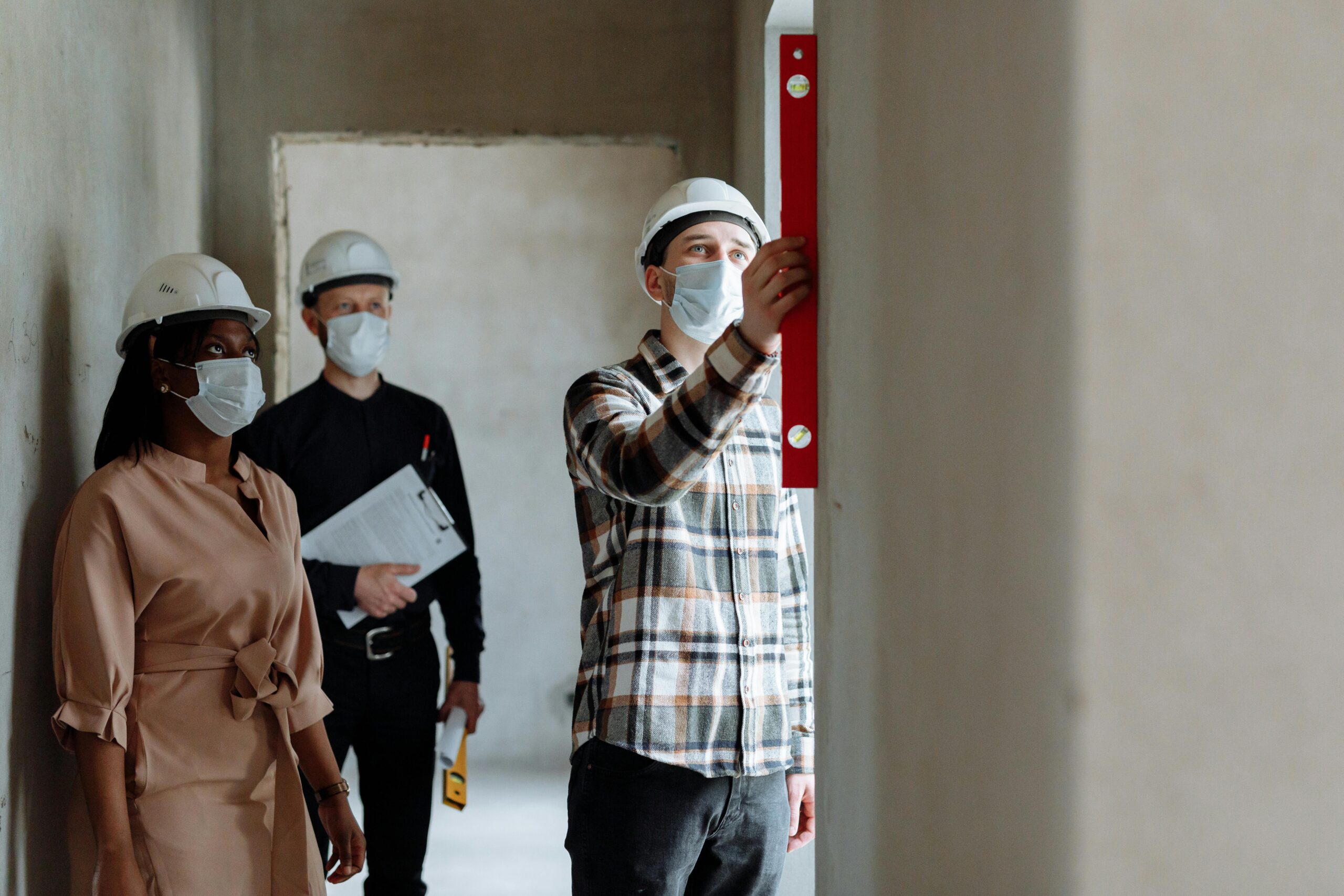 Team of construction workers in hard hats and masks inspecting indoors using a level.